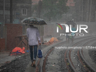 People walk on the railway line with umbrellas in the heavy rain in Dhaka, Bangladesh, on September 15, 2024. (