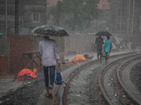 People walk on the railway line with umbrellas in the heavy rain in Dhaka, Bangladesh, on September 15, 2024. (