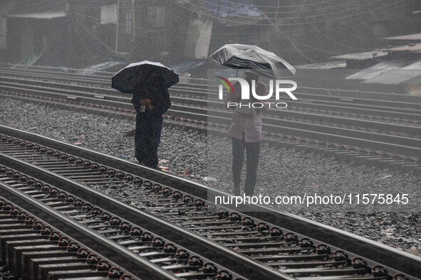 People walk on the railway line with umbrellas in the heavy rain in Dhaka, Bangladesh, on September 15, 2024. 