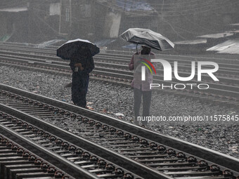 People walk on the railway line with umbrellas in the heavy rain in Dhaka, Bangladesh, on September 15, 2024. (