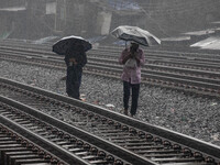 People walk on the railway line with umbrellas in the heavy rain in Dhaka, Bangladesh, on September 15, 2024. (