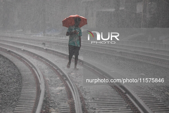 A man walks on the railway line with umbrellas in the heavy rain in Dhaka, Bangladesh, on September 15, 2024. 