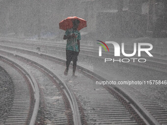 A man walks on the railway line with umbrellas in the heavy rain in Dhaka, Bangladesh, on September 15, 2024. (