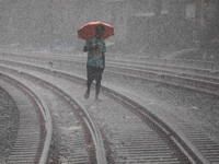 A man walks on the railway line with umbrellas in the heavy rain in Dhaka, Bangladesh, on September 15, 2024. (