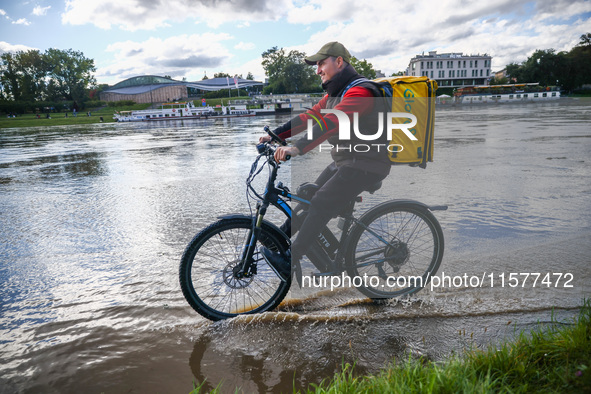 Food delivery courier rides a bicycle after heavy rainfall rised the level of the Vistula River flooding a part of the boulvards in Krakow,...