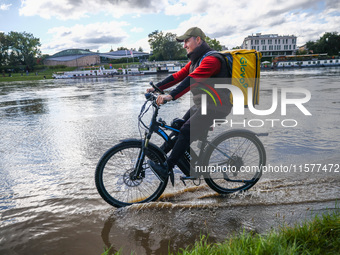 Food delivery courier rides a bicycle after heavy rainfall rised the level of the Vistula River flooding a part of the boulvards in Krakow,...