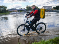 Food delivery courier rides a bicycle after heavy rainfall rised the level of the Vistula River flooding a part of the boulvards in Krakow,...