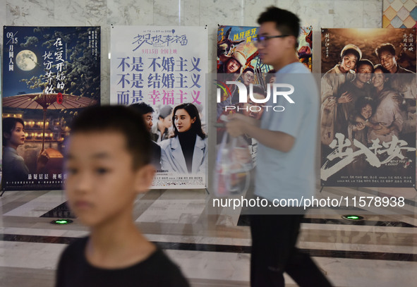 People walk past movie posters at a cinema in Fuyang, China, on September 16, 2024. 