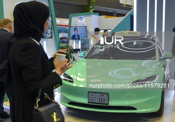 A visitor takes a picture of a Tesla taxi car at the Qatar Mowasalat Pavilion at the ConteQ Expo24 (Advanced Technology for Construction & S...