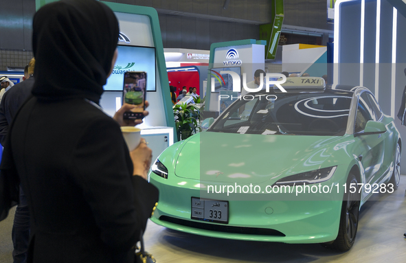 A visitor takes a picture of a Tesla taxi car at the Qatar Mowasalat Pavilion at the ConteQ Expo24 (Advanced Technology for Construction & S...