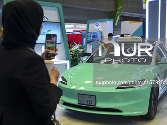 A visitor takes a picture of a Tesla taxi car at the Qatar Mowasalat Pavilion at the ConteQ Expo24 (Advanced Technology for Construction & S...