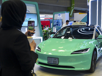 A visitor takes a picture of a Tesla taxi car at the Qatar Mowasalat Pavilion at the ConteQ Expo24 (Advanced Technology for Construction & S...