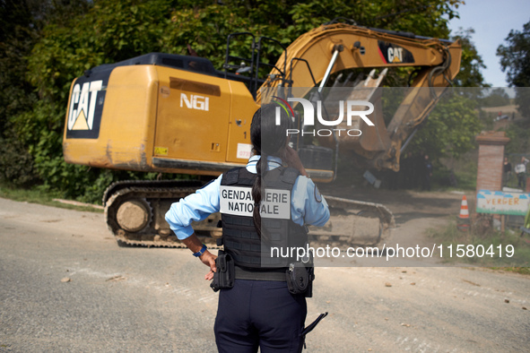 A gendarme looks at an excavator entering the 'Verger' to destroy it. After months of negotiations and pressures from NGE/Atosca, and two in...