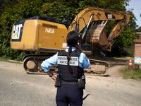 A gendarme looks at an excavator entering the 'Verger' to destroy it. After months of negotiations and pressures from NGE/Atosca, and two in...