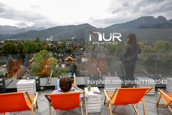 People in warm jackets watch a panorama view on Tatra mountains on a landmark Krupowki Street in the center of Zakopane, a popular Tatra mou...