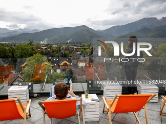 People in warm jackets watch a panorama view on Tatra mountains on a landmark Krupowki Street in the center of Zakopane, a popular Tatra mou...