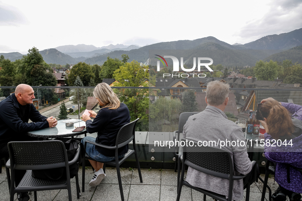 People in warm jackets watch a panorama view on Tatra mountains on a landmark Krupowki Street in the center of Zakopane, a popular Tatra mou...