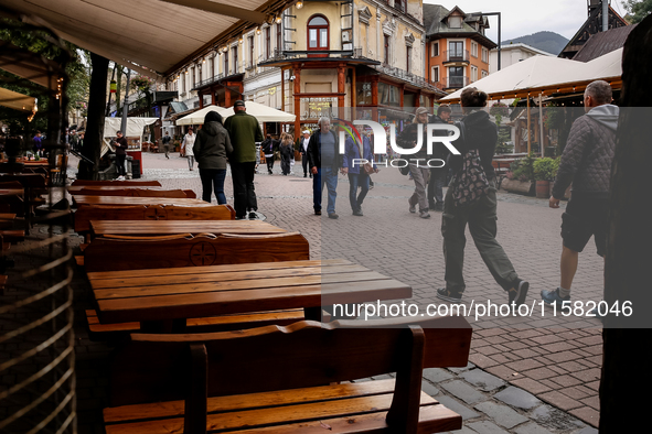 People in warm jackets walk on a landmark Krupowki Street as outdoor restaurants are empty in the center of Zakopane, a popular Tatra mounta...