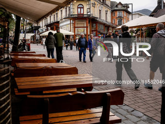 People in warm jackets walk on a landmark Krupowki Street as outdoor restaurants are empty in the center of Zakopane, a popular Tatra mounta...