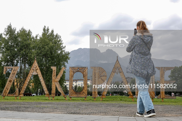 A woman takes a photo of Zakopane sign and a mountain range in the center of Zakopane, a popular Tatra mountain holiday resort as Autumn col...