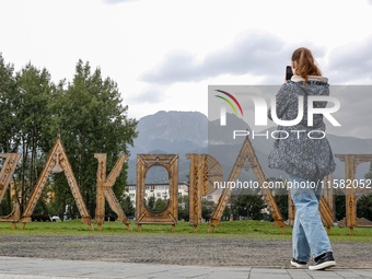 A woman takes a photo of Zakopane sign and a mountain range in the center of Zakopane, a popular Tatra mountain holiday resort as Autumn col...