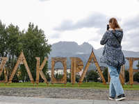 A woman takes a photo of Zakopane sign and a mountain range in the center of Zakopane, a popular Tatra mountain holiday resort as Autumn col...