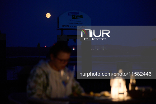 People are seen dining out as the Harvest Moon is seen in the night sky over Frankfurt an der Oder, Germany on 17 September, 2024. 