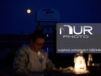 People are seen dining out as the Harvest Moon is seen in the night sky over Frankfurt an der Oder, Germany on 17 September, 2024. (