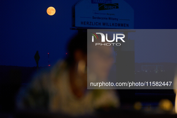 People are seen dining out as the Harvest Moon is seen in the night sky over Frankfurt an der Oder, Germany on 17 September, 2024. 