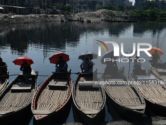 Boatmen hold umbrellas under the hot sun as they wait for passengers at the old Buriganga River channel in Dhaka, Bangladesh, on September 1...