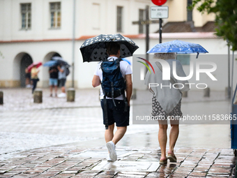 People with umbrellas walk in the rain on the street in Krakow, Poland, on August 21, 2024. (