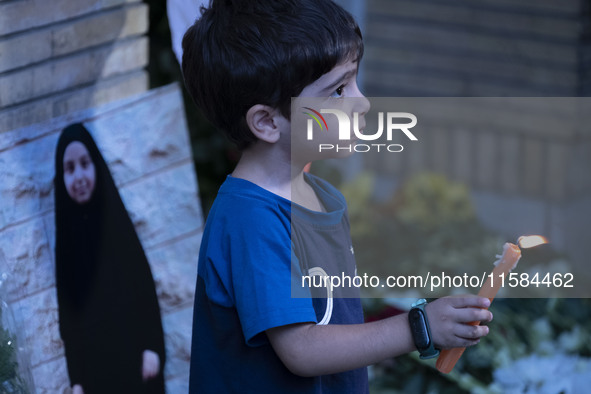 A young Iranian boy holds a candle next to a portrait of a young Lebanese girl who is killed in a deadly pager attack, while standing in fro...