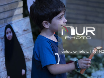 A young Iranian boy holds a candle next to a portrait of a young Lebanese girl who is killed in a deadly pager attack, while standing in fro...