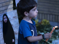 A young Iranian boy holds a candle next to a portrait of a young Lebanese girl who is killed in a deadly pager attack, while standing in fro...