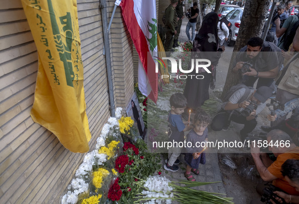 Iranian children hold candles next to a portrait of a young Lebanese girl who is killed in a deadly pager attack, while standing in front of...