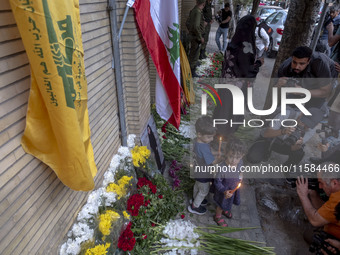 Iranian children hold candles next to a portrait of a young Lebanese girl who is killed in a deadly pager attack, while standing in front of...