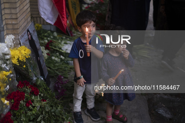 Iranian children hold candles next to a portrait of a young Lebanese girl who is killed in a deadly pager attack, while standing in front of...