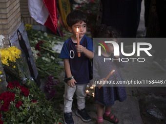 Iranian children hold candles next to a portrait of a young Lebanese girl who is killed in a deadly pager attack, while standing in front of...