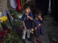 Iranian children hold candles next to a portrait of a young Lebanese girl who is killed in a deadly pager attack, while standing in front of...