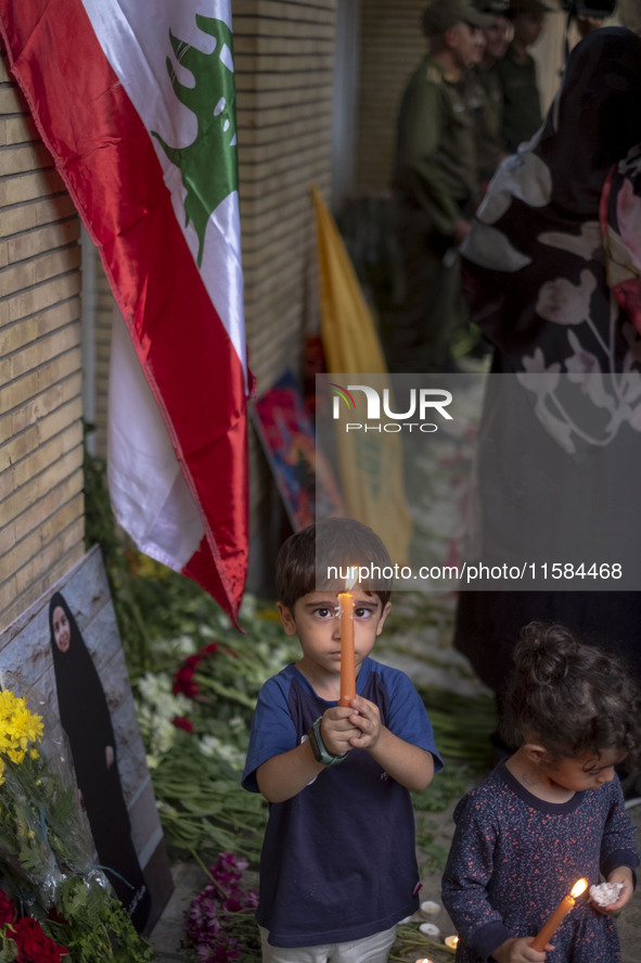 Iranian children hold candles next to a portrait of a young Lebanese girl who is killed in a deadly pager attack, while standing in front of...