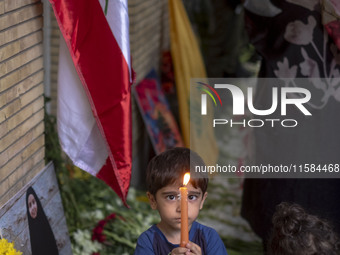 Iranian children hold candles next to a portrait of a young Lebanese girl who is killed in a deadly pager attack, while standing in front of...