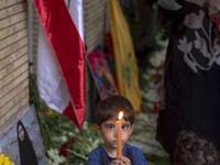 Iranian children hold candles next to a portrait of a young Lebanese girl who is killed in a deadly pager attack, while standing in front of...