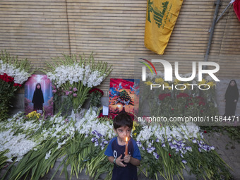 A young Iranian boy holds a candle while standing next to portraits of a young Lebanese girl who is killed in a deadly pager attack, a flag...