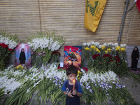 A young Iranian boy holds a candle while standing next to portraits of a young Lebanese girl who is killed in a deadly pager attack, a flag...