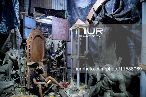 A boy takes his mobile phone in front of an idol of the Hindu goddess Durga in Kumartuli, the potter's village in Kolkata, India, on Septemb...