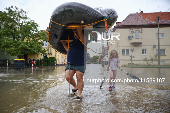 A man with a girl carries a raft after Nysa Klodzka river flooded town of Lewin Brzeski in southwestern Poland, on September 19th, 2024. Sto...