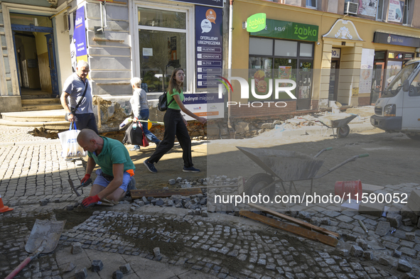 People walk past a worker repairing the pavement in the flood-hit town of Glucholazy, Poland, on September 20, 2024. 