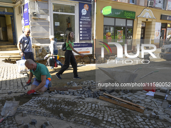 People walk past a worker repairing the pavement in the flood-hit town of Glucholazy, Poland, on September 20, 2024. (