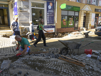 People walk past a worker repairing the pavement in the flood-hit town of Glucholazy, Poland, on September 20, 2024. (