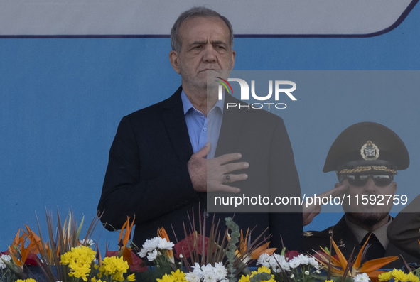 Iranian President Masoud Pezeshkian (C) stands at attention while attending a military parade commemorating the anniversary of the Iran-Iraq...